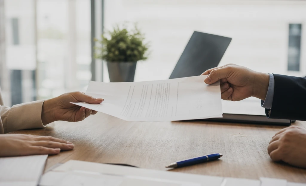 Two people passing a signed document across an office desk